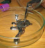 A silvery molasses-like liquid being poured into a circular container with a height equivalent to a smaller coin on its edge