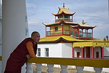 Buddhist monk in Siberia in robes leaning on railing looking at temple