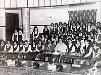 Black-and-white photo of Saddam Hussein, in a suit, with a group of women students
