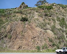 Photograph of a rock formation with a road and a car at its bottom.
