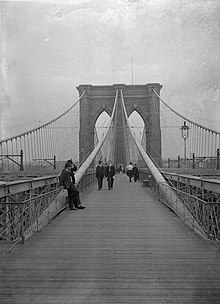 A black-and-white view of the Brooklyn Bridge in 1899 looking east on the pedestrian walkway
