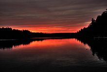 Orillas boscosas del lago recortadas contra el cielo de color rojo oscuro