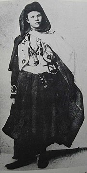 A black and white photograph of a young woman, wearing an assortment of Arabic styled clothing