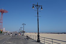 Original street lights, similar to those installed on Fifth Avenue in Manhattan. They consist of stylized black poles with two lamps at the top. The boardwalk is on the left and the beach is on the right.