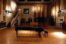 A colour image of a large room with a piano in the middle