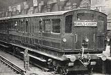 A three-quarter black-and-white photograph of a train standing at a station, showing the end carriage with windows at the end.
