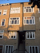 A four-story, brick apartment block showing the building's facade, with several windows and an internal staircase leading into the block.