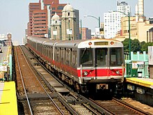 A silver and red rapid transit train departing an above-ground station