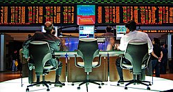 Two traders sit at computer monitors with financial information.