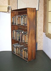 A three shelf timber bookcase, filled with books, stands at an angle in front of a doorway to the Secret Annexe