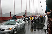 A group of bicyclist following a car.