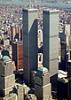 Aerial view of two 110-story twin towers; the building have gray, steel exteriors, and the structure on the left is topped by a large antenna. Several skyscrapers are visible surrounding the two towers.