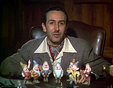 Walt Disney sits in front of a set of models of the seven dwarfs
