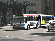 A white bus in two sections, connected by a black expansion joint, goes into a turn.
