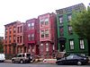 A group of five three-story brick rowhouses, two and three bays wide, on an urban street. The one on the right is painted green, the three in the middle have projecting bays on the upper stories and the leftmost one is unpainted.