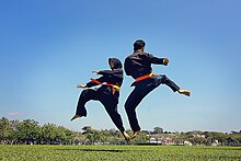 A woman and a man in black outfits with red belts practising the martial art of Silat Melayu