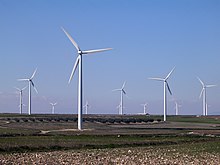 A wind farm of about a dozen three-bladed white wind turbines.