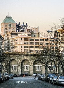 A stone viaduct approach ramp to the Brooklyn Bridge, as seen from a street in Brooklyn, with buildings to either side