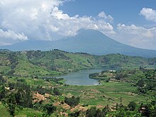 Photograph of a lake with one of the Virunga mountains behind, partially in cloud