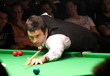 Ronnie O'Sullivan playing a snooker shot at a snooker competition with a crowd watching him