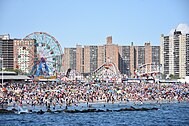 Concurrida playa de Coney Island con noria y montaña rusa en segundo plano.