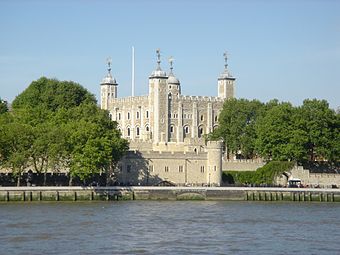 A huge square tower of grey stone is seen beyond fortifications on the edge of a river.