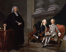Conversation piece in oils: Ayscough dressed in black with a clerical collar stands beside a settee on which the two boys sit, one wearing a grey suit the other a blue one. He holds a sheet of paper; the boys hold a book.