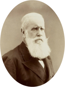 Retrato fotográfico de medio cuerpo de un hombre mayor con cabello blanco y barba vestido con una chaqueta oscura y corbata