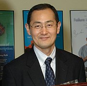 upper-body shot of young man smiling, wearing glasses with dark suit and tie