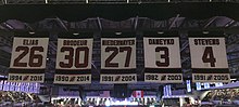 Five banners with the New Jersey Devils retired numbers, showing the player surname and years with the team: Eilias, 26, 1994–2016; Brodeur, 30 1990–2014; Niedermayer, 27, 1991–2004; Daneyko, 3, 1982–2003; and Stevens, 4, 1991–2005.
