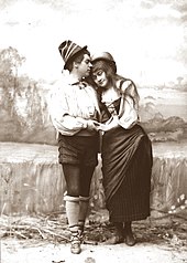 black and white photograph of young white woman in 16th-century peasant costume, embraced by young man also in period dress