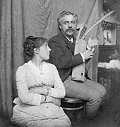 youngish couple in informal pose; the man is holding a small harp, the woman is looking at him