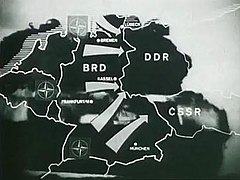 Outline map of Belgium, the Netherlands, West Germany, East Germany and Czechoslovakia with arrows indicating the direction of a hypothetical NATO attack from West Germany into East Germany and Czechoslovakia. An advancing tank is shown in the background behind the map.